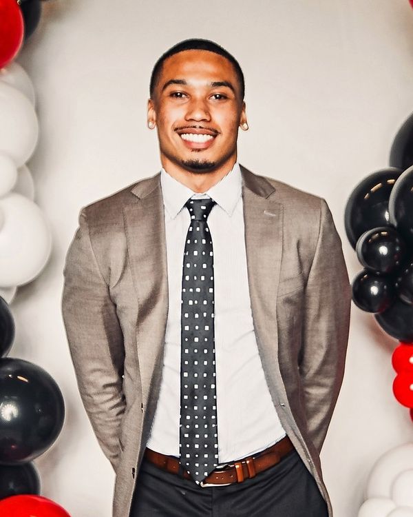 Devynn smiling in a grey blazer, white shirt and dotted tie