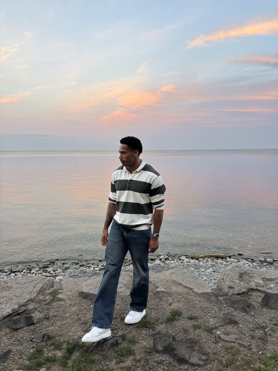 Devynn in a striped rugby shirt walking along a rocky shoreline at sunset