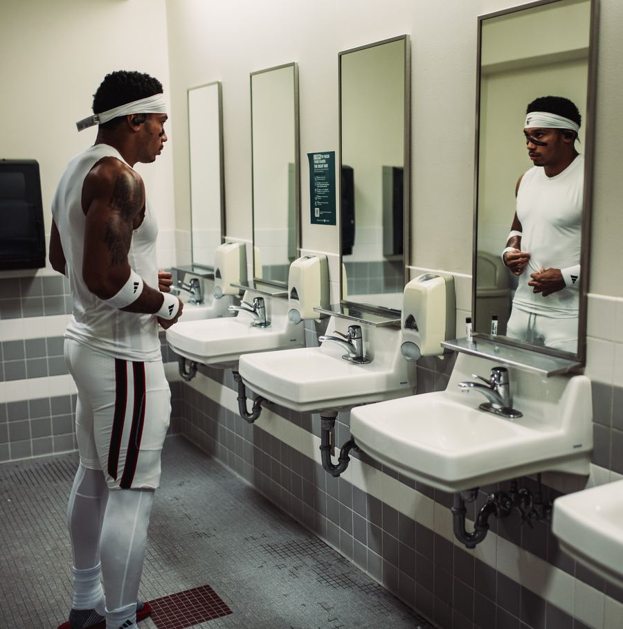 Devynn in white game gear checking himself in a locker room mirror